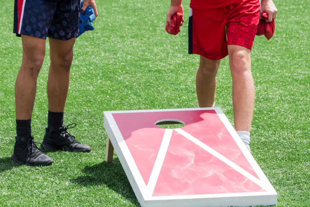 Two people playing cornhole outside on a red board.